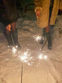 two people standing in the snow with sparklers coming out of their legs and feet