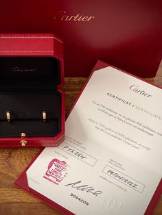 an open red box with two gold rings in it next to a certificate on a wooden table