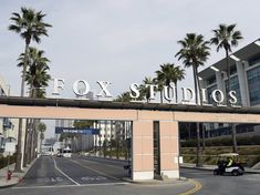 the entrance to fox studios with palm trees in the foreground and a police car driving down the street