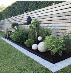 an outdoor garden with white balls and greenery in the center, along side a wooden fence