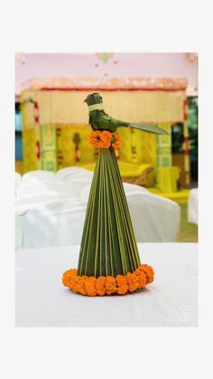 a green bird sitting on top of a flowered cone with orange flowers around it