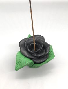 a black rose sitting on top of a green leaf with a stick sticking out of it