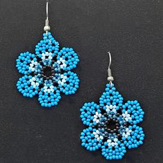 blue and white beaded flower earrings on black surface with silver earwires hanging from hooks