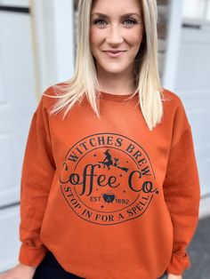 a woman with blonde hair wearing an orange sweatshirt that says witch's brew coffee co