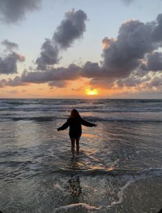 a woman standing in the ocean at sunset