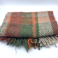 an orange, green and white blanket laying on top of each other with fringes