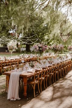 a long table is set up for an outdoor wedding with white and pink flowers hanging from the branches