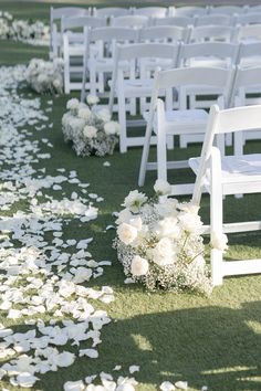 the aisle is lined with white chairs and petals on the grass, as well as flowers