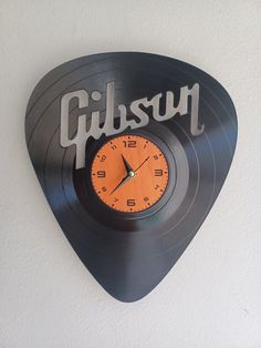 a clock with the word gibson written on it and an orange hand - painted guitar pick