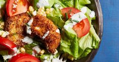 a salad with chicken, tomatoes and corn on it in a metal bowl sitting on a blue surface