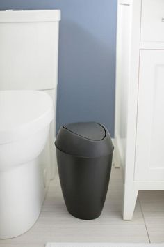 a black trash can sitting next to a white toilet in a blue and white bathroom