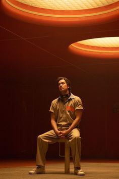 a man sitting on top of a wooden bench in front of a red wall and two circular lights