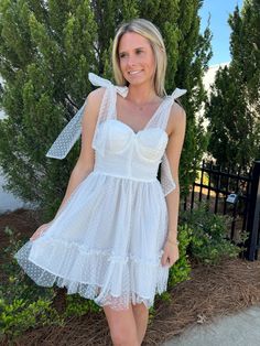 Our FANCY ivory tie strap dress is designed with a fitted bodice adorned with polka dots, sheer bow tie straps on the shoulder, a knee-length skirt with ruffling, and finished with comprehensive beading. She is prefect for brides and grads this season. Tie adjustable straps adjustable straps fitted bodice This sweatshirt fits true to size Model is 5'2" with a 32" bust, 25" waist, and 31" hips wearing a Small Polka Dot Spaghetti Strap Dress With Ruffles, Polka Dot Dress With Ruffles And Spaghetti Straps, Flirty Dresses With Bow And Ruffled Straps, White Flirty Dress With Bow Straps, White Swiss Dot Party Dress, Polka Dot Ruffled Wedding Dress, Feminine Sleeveless Swiss Dot Dress, Feminine Swiss Dot Sleeveless Dress, Summer Polka Dot Dress For Wedding