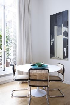 a white table and chairs in front of a large window with an abstract painting on the wall