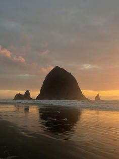 the sun is setting on an ocean beach with rocks in the water and one large rock sticking out of the water