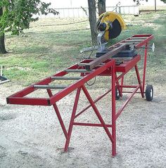 a machine that is sitting on top of a red stand in the dirt next to a tree