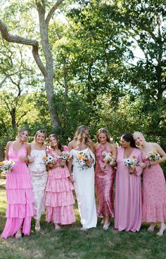 a group of women standing next to each other in pink and white dresses on the grass