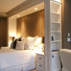 a white bed sitting next to a tall book shelf in a room with brown walls