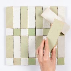 a woman is painting a wall with green and white tiles on the wall, while another hand holds a paint roller in front of it