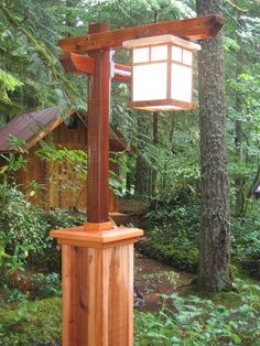 a wooden post with a lantern on top in the woods next to some trees and bushes