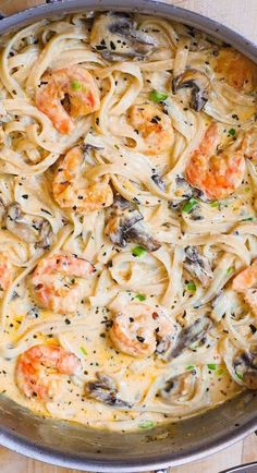 pasta with shrimp and mushrooms in a skillet on a wooden table next to utensils