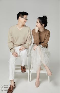 two people sitting next to each other on a white bench and one person is wearing a brown sweater