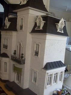 a white doll house with black roof and windows on the top floor in front of a window