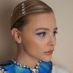 a woman with blue and white makeup wearing a necklace