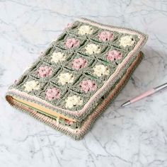 a crocheted notebook cover sitting on top of a marble table next to a pen