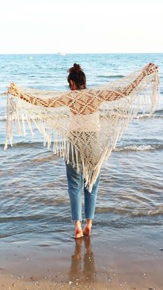 a woman is standing on the beach with a white shawl over her shoulders and feet in the water