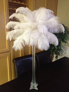 a tall vase filled with white feathers sitting on top of a black dining room table