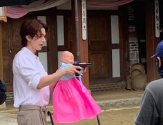 a man holding a baby doll in front of a building with other people standing around