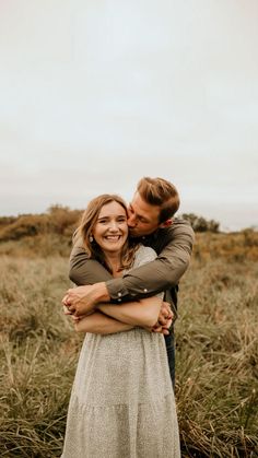 a man and woman hugging each other in the middle of a field with tall grass