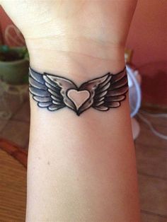 a wrist tattoo with a heart and wings on it