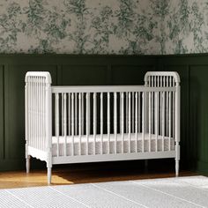 a white crib in a room with green wallpaper