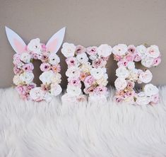 the word easter spelled with flowers and bunny ears on a fluffy white surface in front of a wall