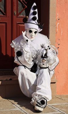 a man dressed in white and black sitting on the ground next to a red door