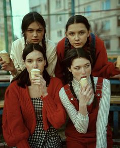 three women sitting on a bench eating donuts and drinking coffee while one woman looks at the camera