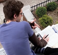 a man is sitting on a bench and looking at something in his hand as he writes