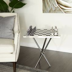 a white chair sitting next to a table with chess pieces on top of it in front of a plant