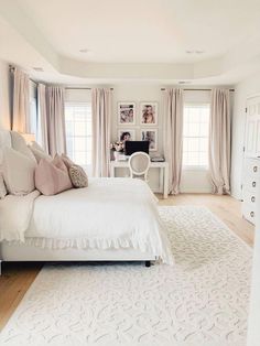 a white bed sitting in a bedroom on top of a hard wood floor next to two windows