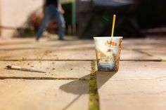 a cup with a straw in it sitting on the ground next to a person walking