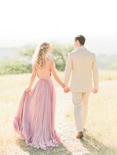 a man and woman holding hands while walking through the grass