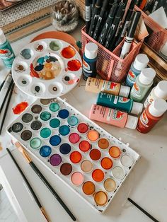 an assortment of paints and brushes on a table with other art supplies in the background