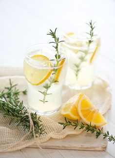 two glasses filled with lemonade and rosemary garnish on a cloth covered table