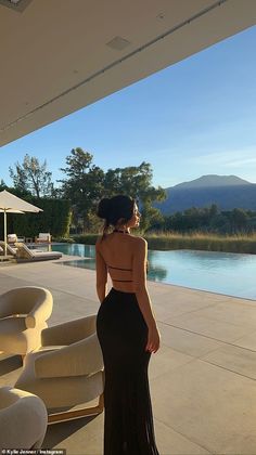 a woman standing in front of a swimming pool wearing a black dress with open back