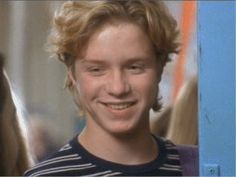 a young man with blonde hair smiling at the camera