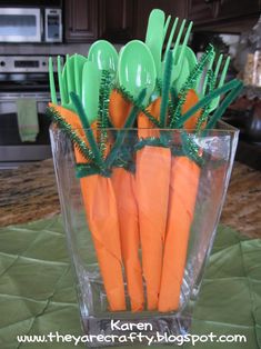 there are plastic forks and carrots in a glass vase on the counter top with green handles