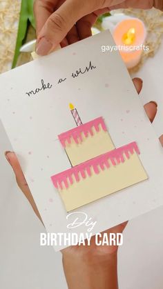 someone holding up a card with a birthday cake on it and candles in the background