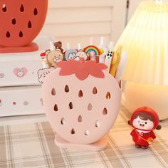 a pink strawberry shaped container sitting on top of a table next to a small figurine